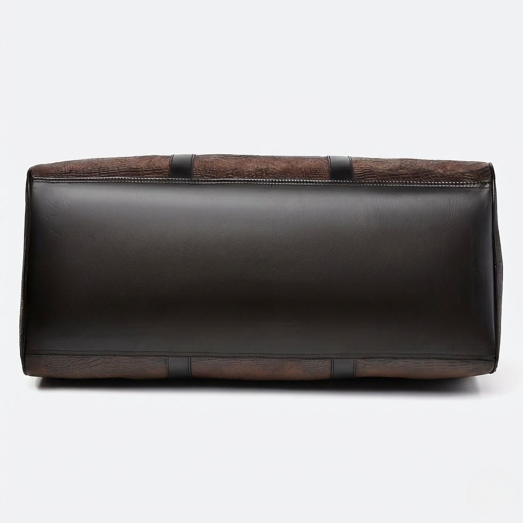 Dessous du sac de voyage effet crocodile, fond en simili cuir noir lisse avec coutures renforcées et bandes noires