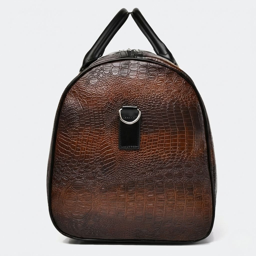 Vue latérale du bagage cabine en simili cuir marron relief crocodile, avec anneau métal pour fixer la bandoulière