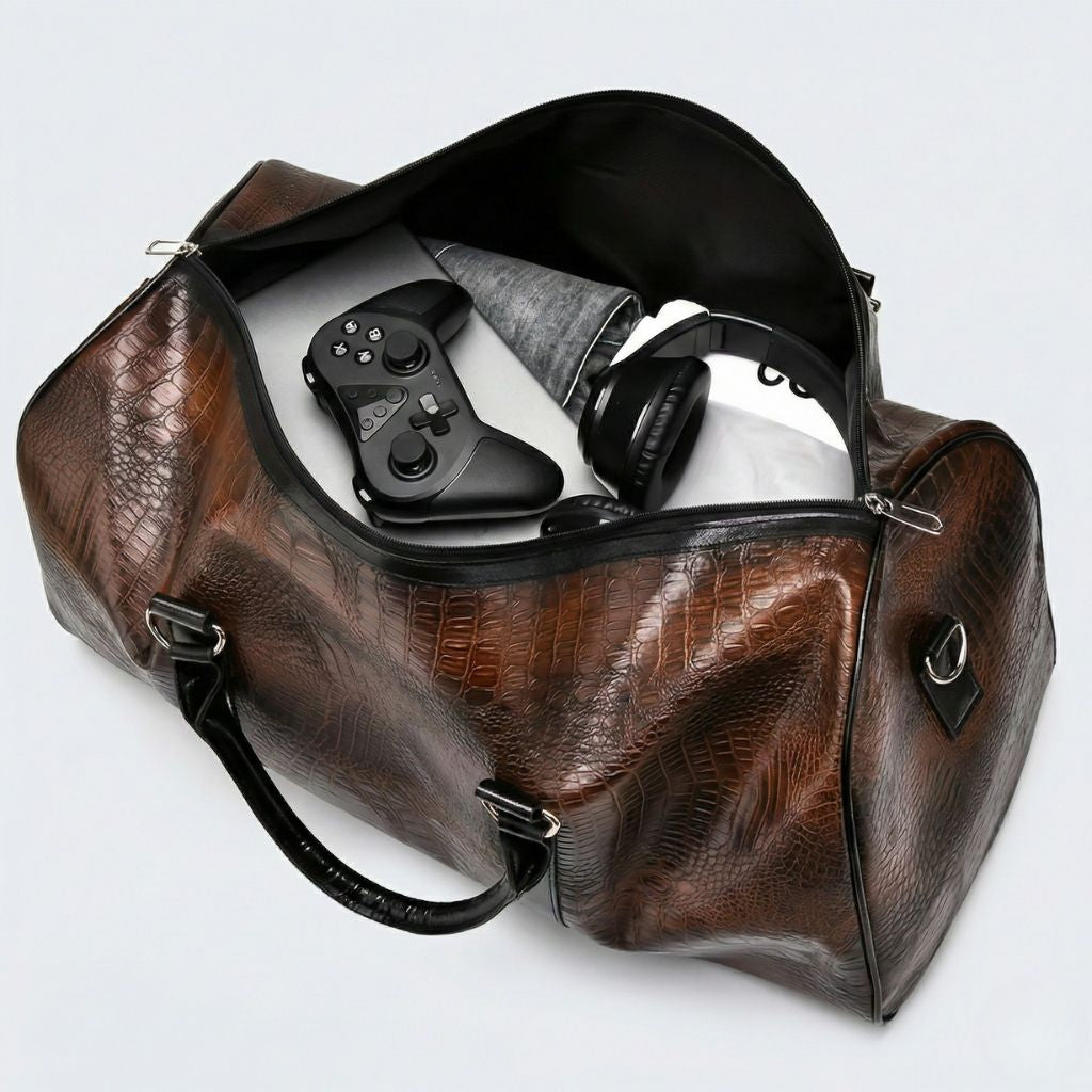 Sac de voyage en simili cuir brun croco ouvert, intérieur noir contenant une manette et un casque audio Image