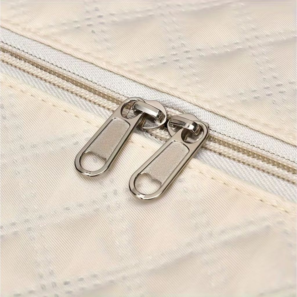 Gros plan des doubles tirettes argentées sur le tissu matelassé diamants blanc crème du sac de voyage