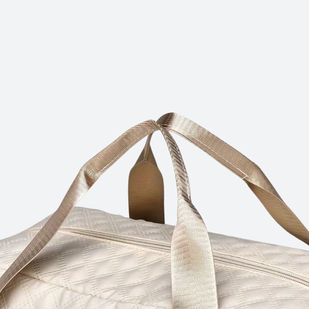 Gros plan des doubles poignées dorées du sac blanc crème sur la fermeture éclair principale du sac