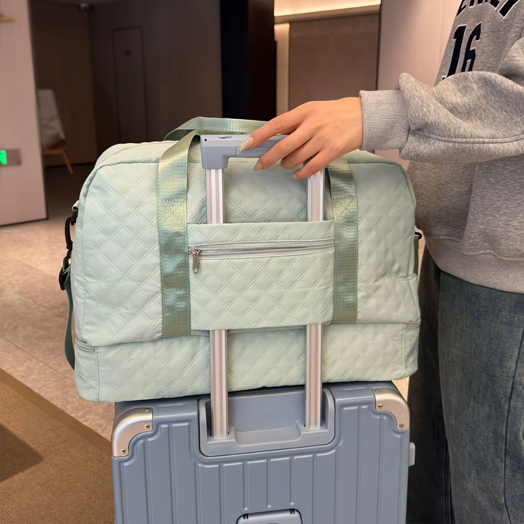 Sac de voyage week-end vert menthe matelassé posé sur la poignée d'une valise grise, pratique pour voyager léger Image