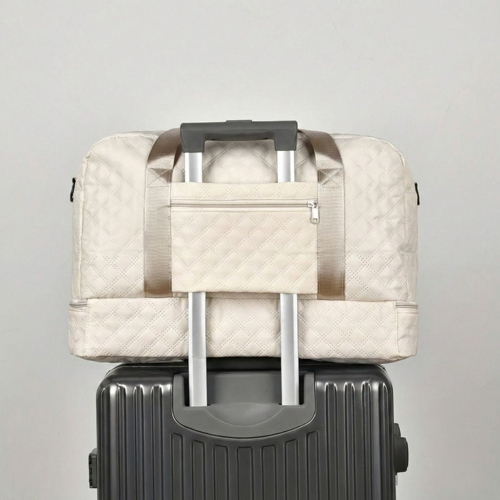 Sac matelassé blanc crème glissé sur la poignée d'une valise noire via le passant trolley intégré au dos