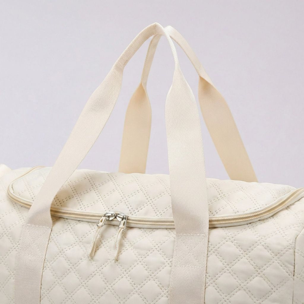 Gros plan du dessus du sac matelassé blanc crème : fermeture éclair argent et doubles poignées larges ivoire