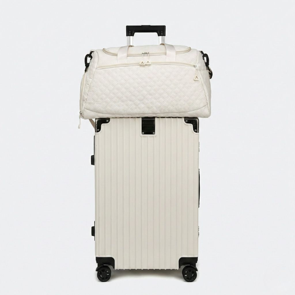Sac de voyage matelassé beige posé sur une valise ivoire à roulettes, parfait pour voyager léger Image