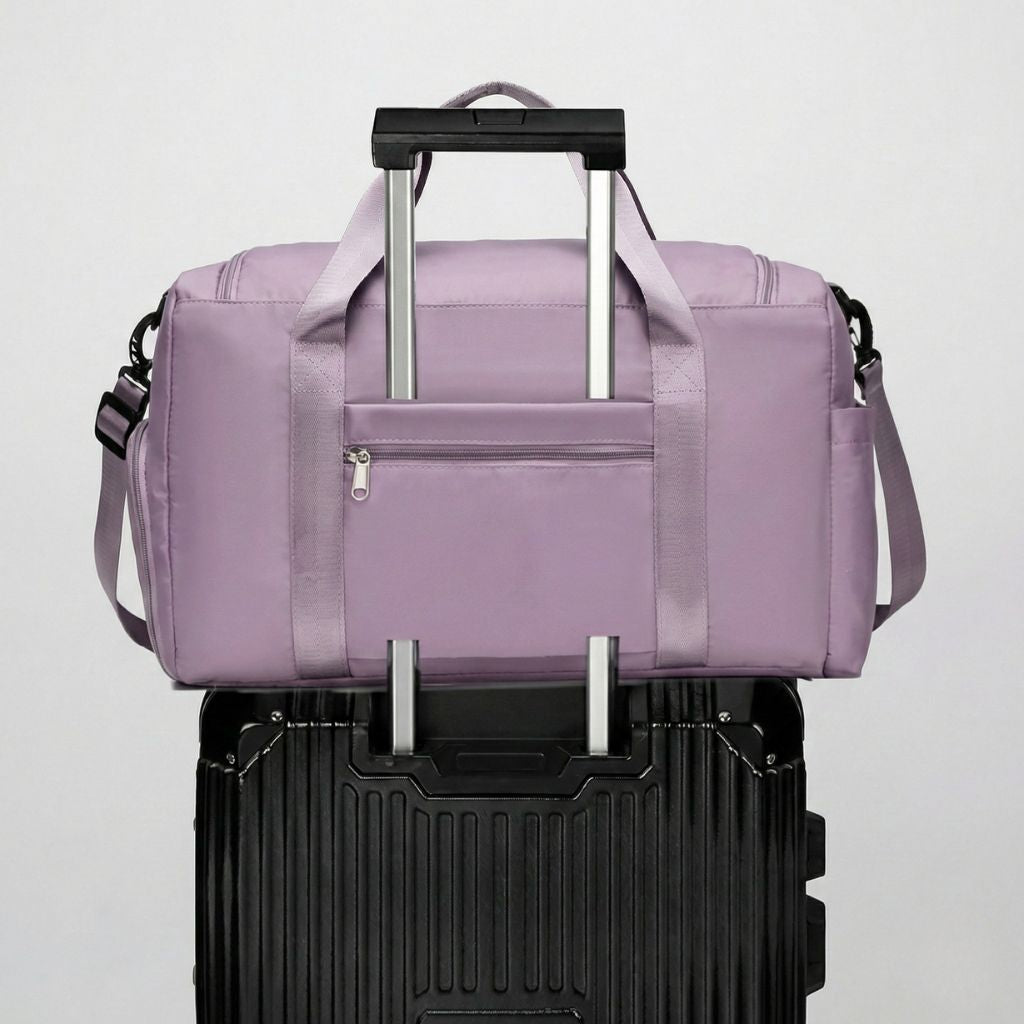 Sac de voyage femme en nylon violet pastel posé sur une valise noire via le passage trolley Image