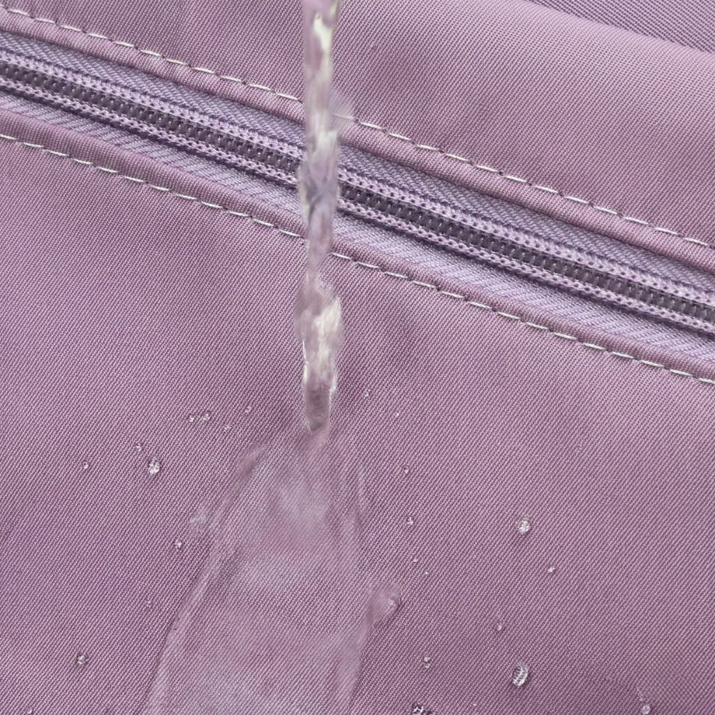 Gros plan sur le tissu imperméable mauve du sac de voyage femme avec un filet d'eau glissant sur la surface