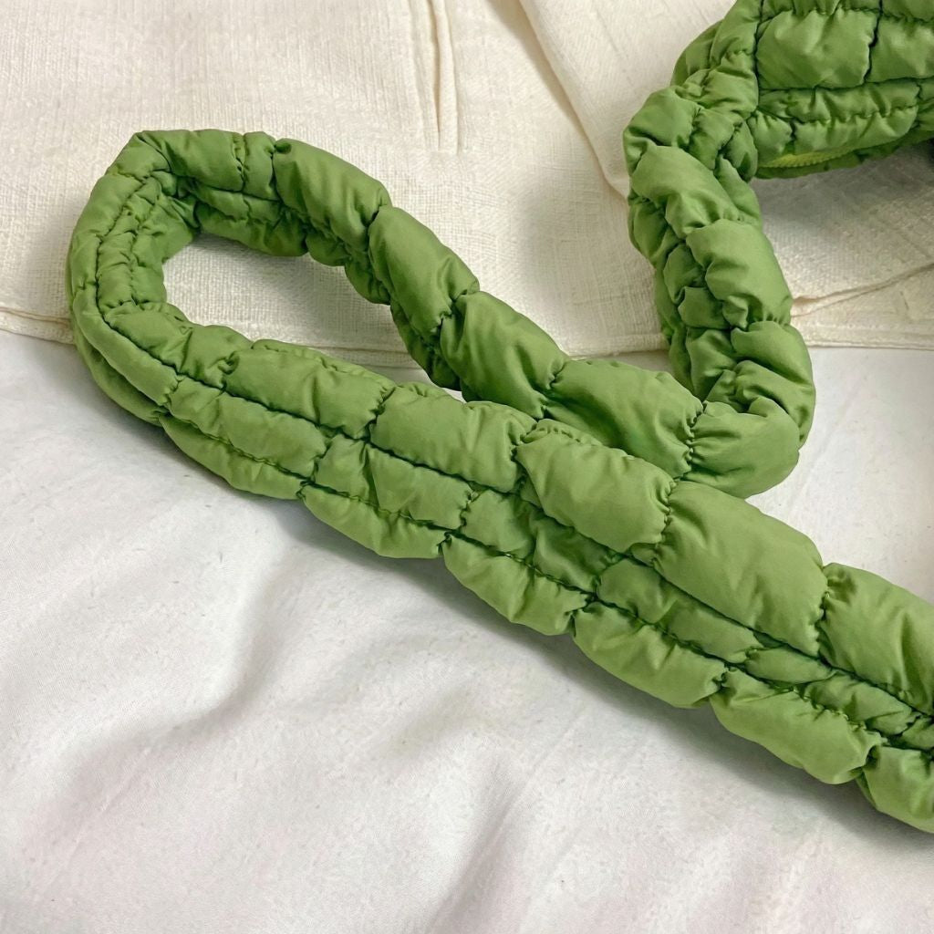 Anse tressée bouffante en nylon matelassé vert anis du sac de voyage femme, posée sur tissu crème