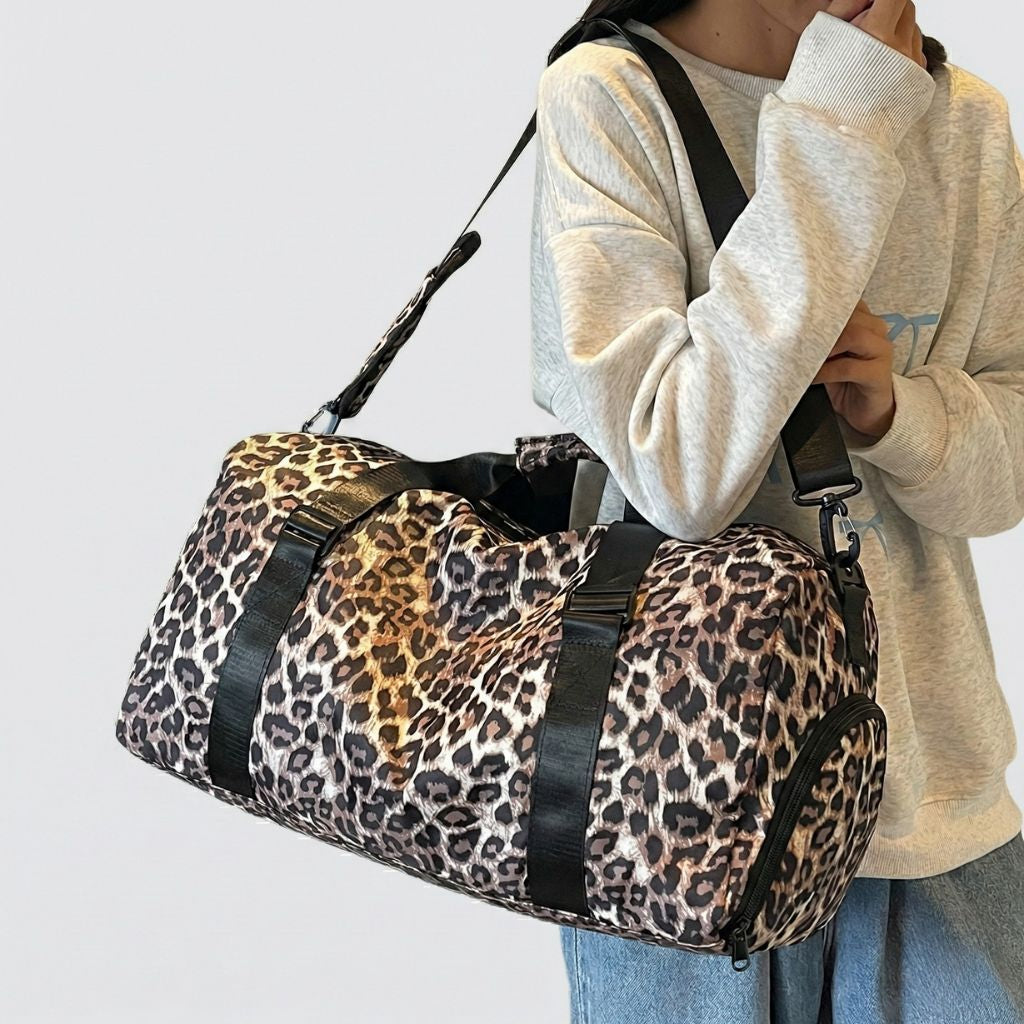 Femme portant sur l'épaule un sac de voyage polochon à imprimé léopard marron et noir avec bandoulière Image