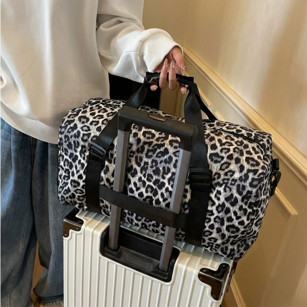 Femme portant un sac week-end léopard blanc et noir à la main dans un couloir, jean et sweat blanc