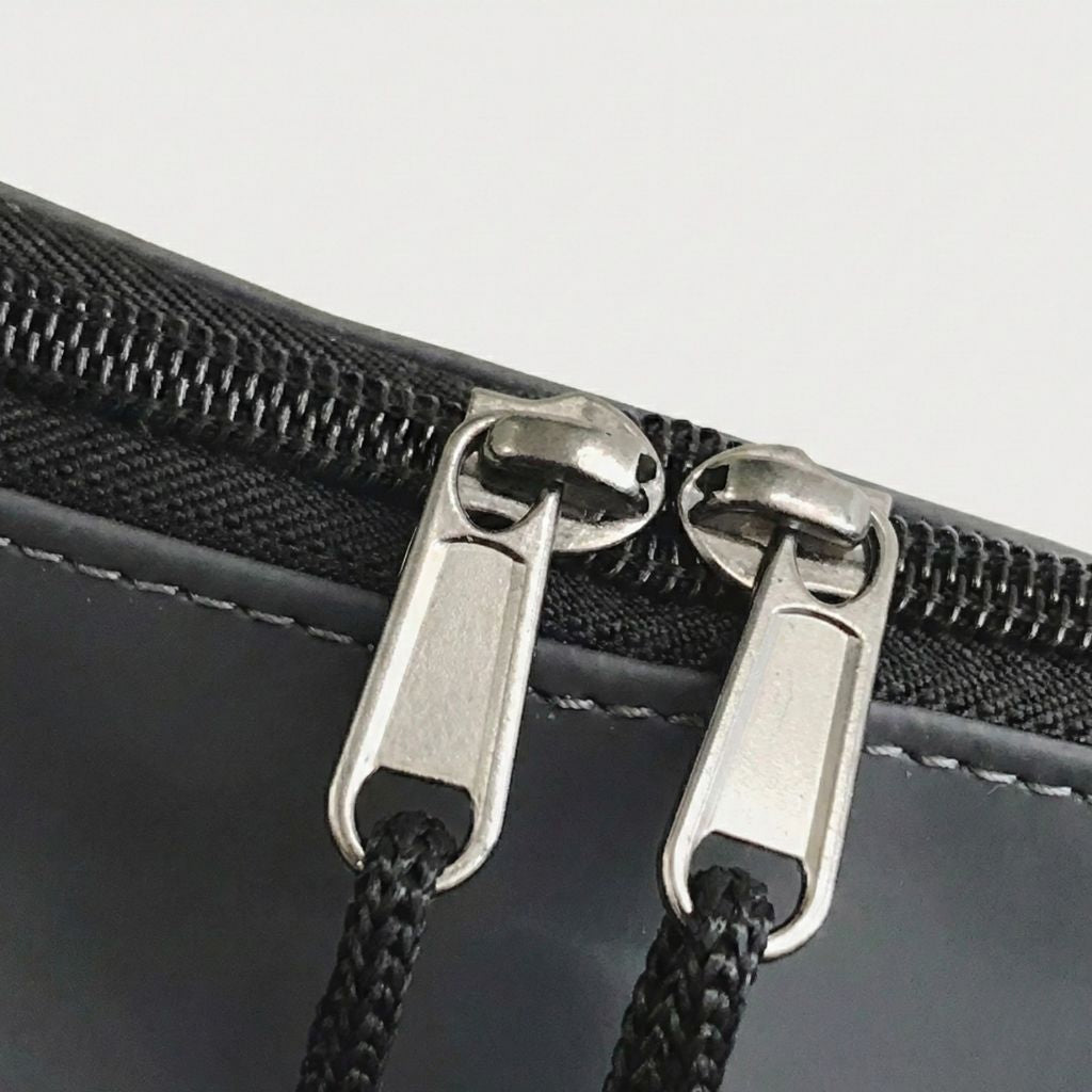 Gros plan des doubles tirettes métal argentées de la fermeture éclair principale du sac de voyage imperméable