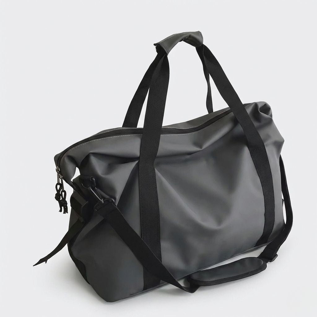 Sac de voyage imperméable noir graphite vue 3/4 avec poignées, bandoulière longue, clips noirs et finition mate