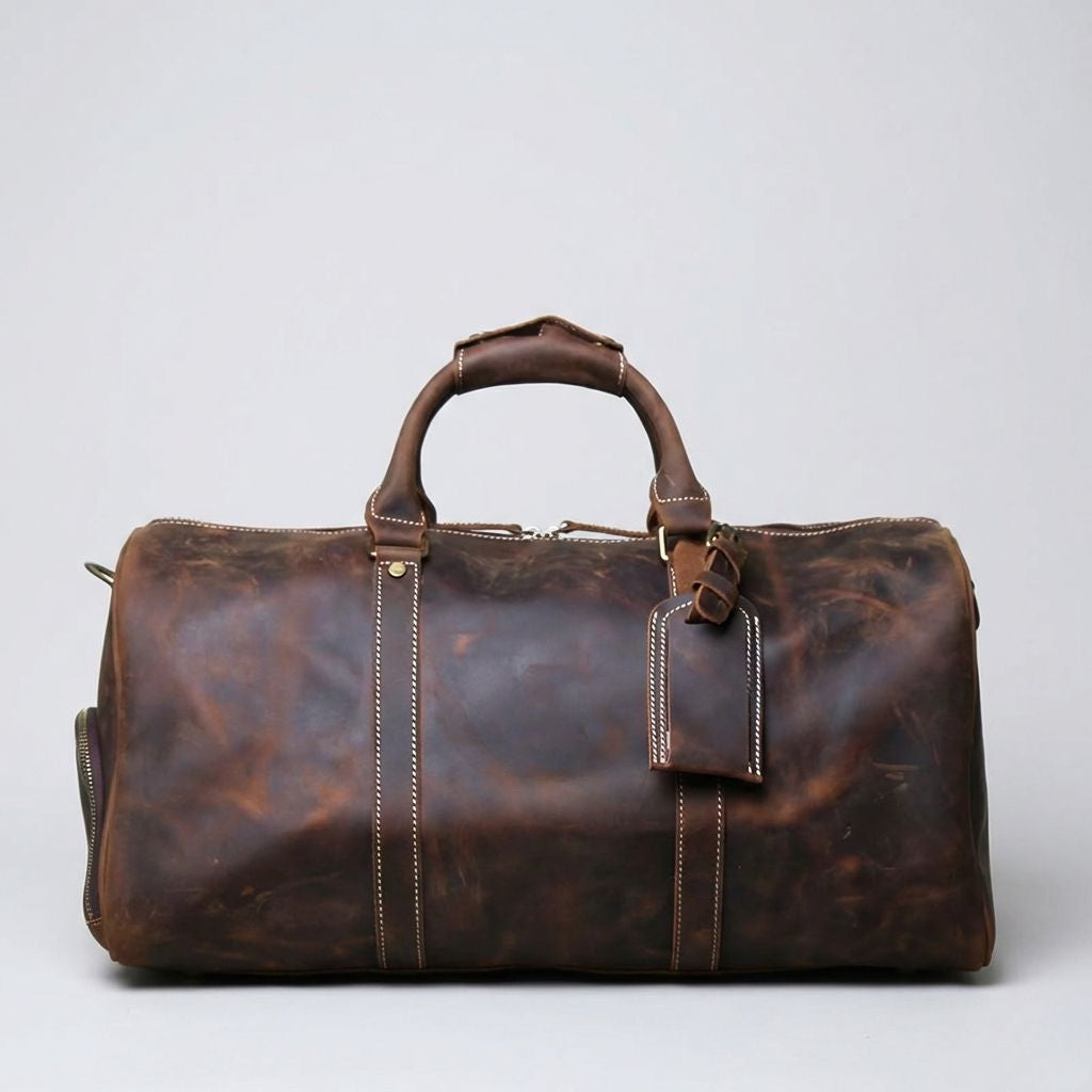 Sac de voyage en cuir marron foncé, étiquette bagage en cuir sur la poignée et coutures blanches contrastées