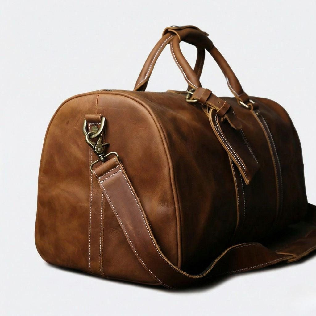 Vue latérale d'un sac de voyage en cuir cognac vintage, détail de l'anneau en laiton et de la bandoulière attachée