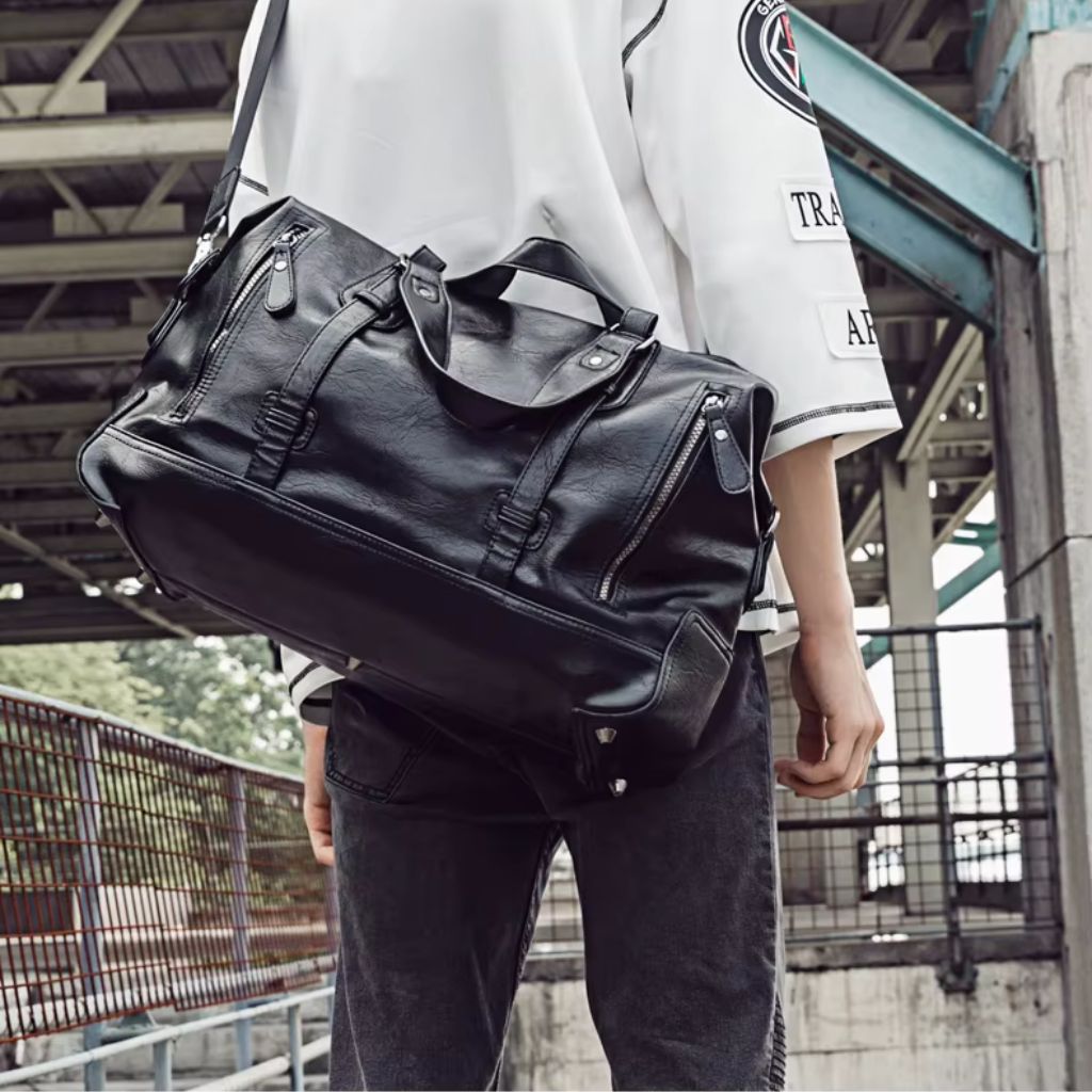 Homme portant le sac de voyage noir en bandoulière sur l'épaule dans une structure industrielle