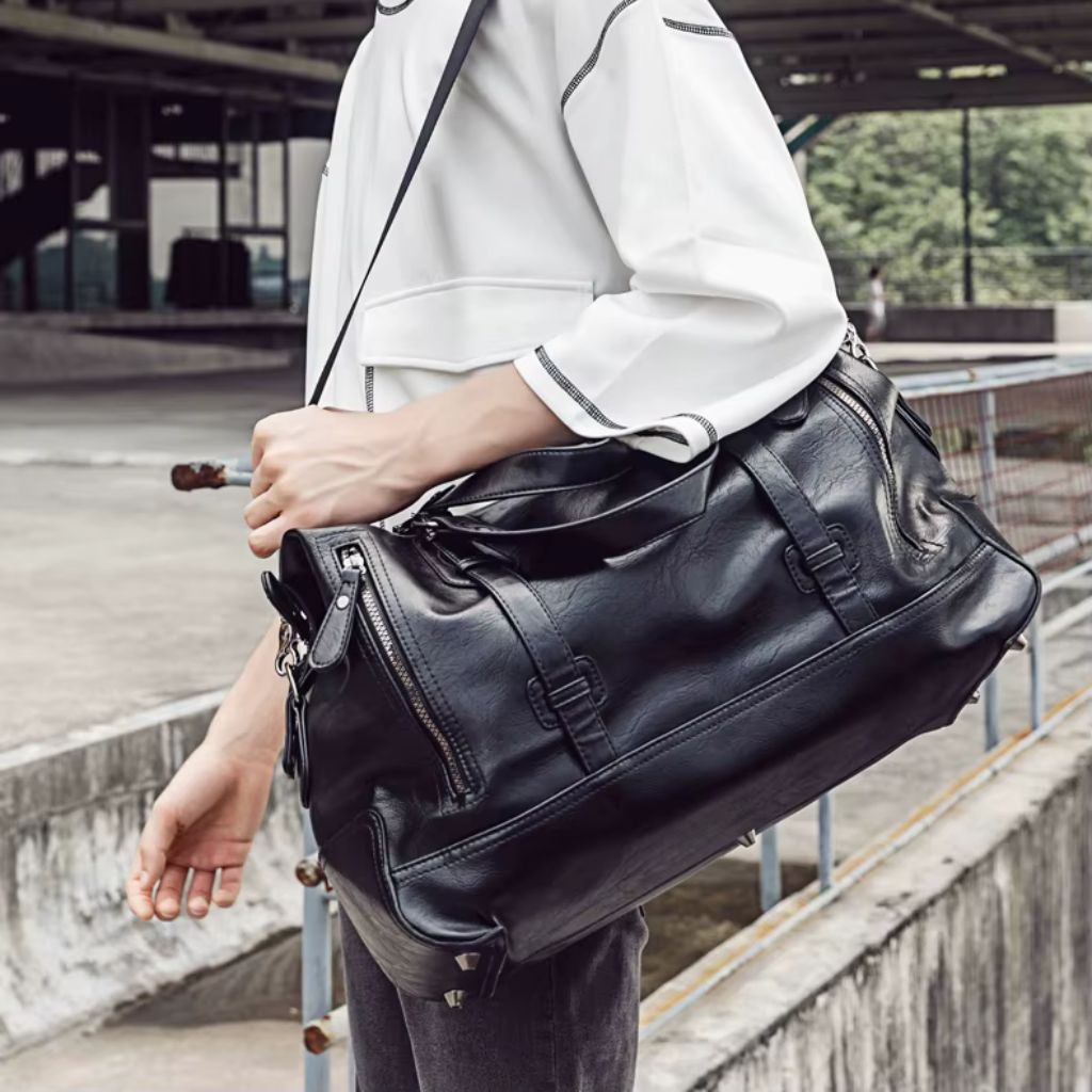 Sac de voyage cabine noir porté à la main par un homme en veste blanche dans un cadre urbain