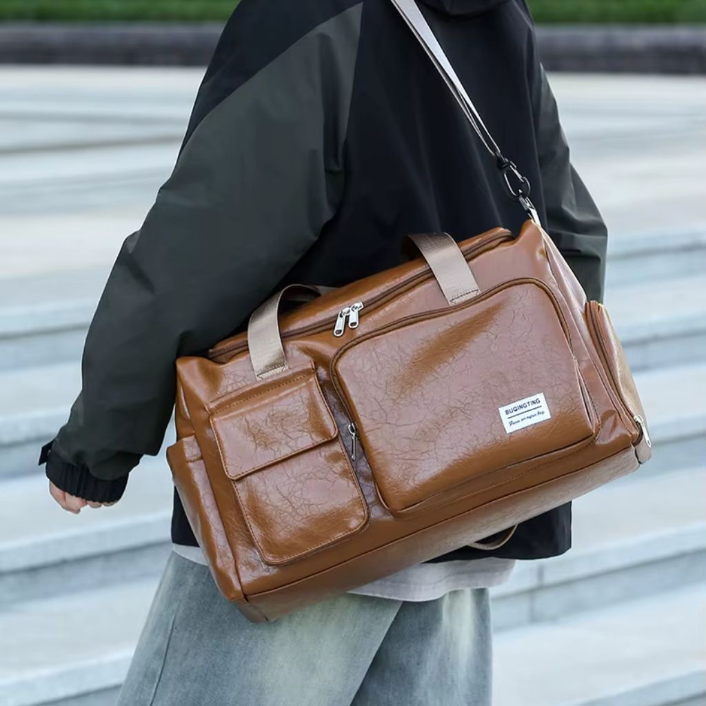 Homme portant le sac cabine cognac vieilli en bandoulière sur l'épaule dans un cadre urbain