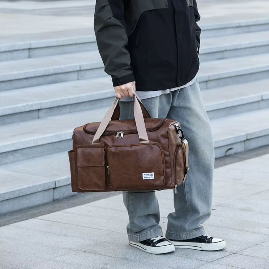 Homme tenant le sac de voyage marron vieilli à la main face à des marches en pierre extérieures