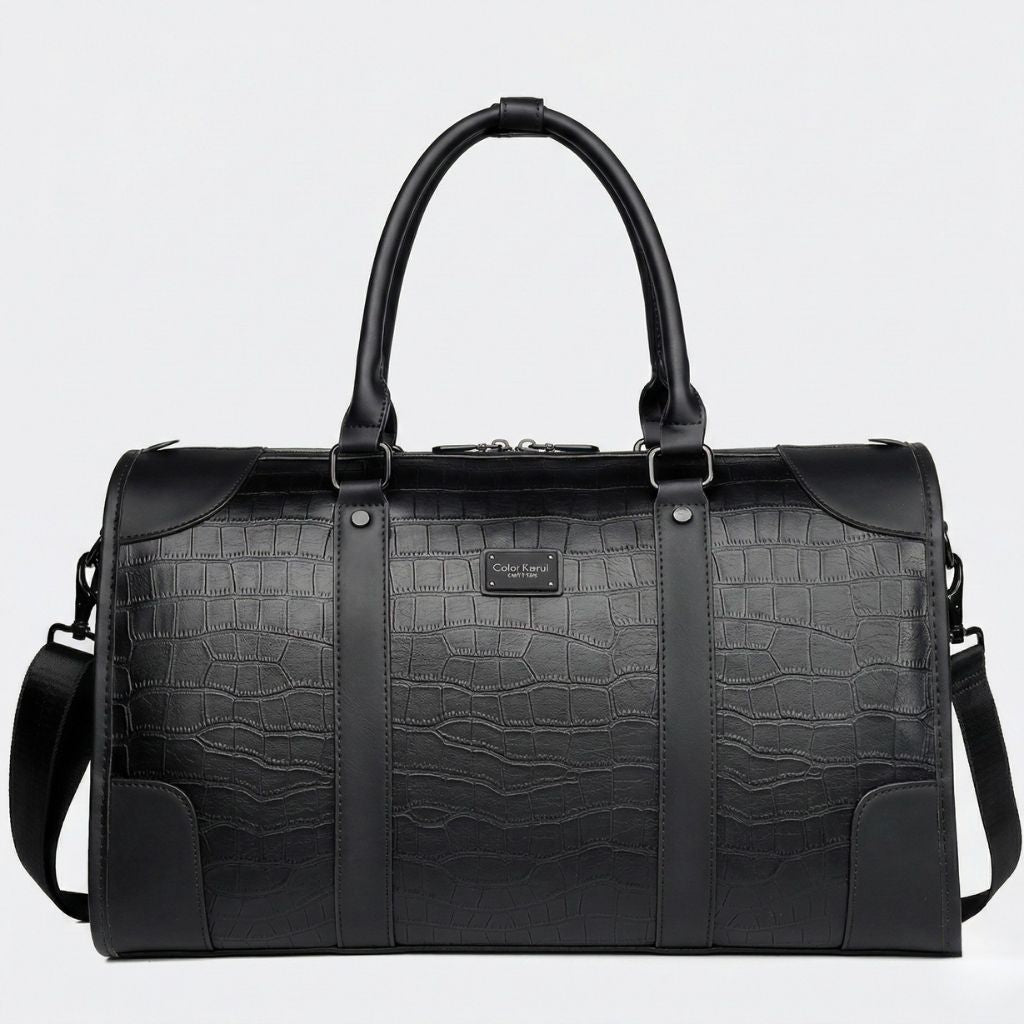 Face avant du sac de voyage noir cabine, motif croco embossé et plaquette métal sur la sangle centrale