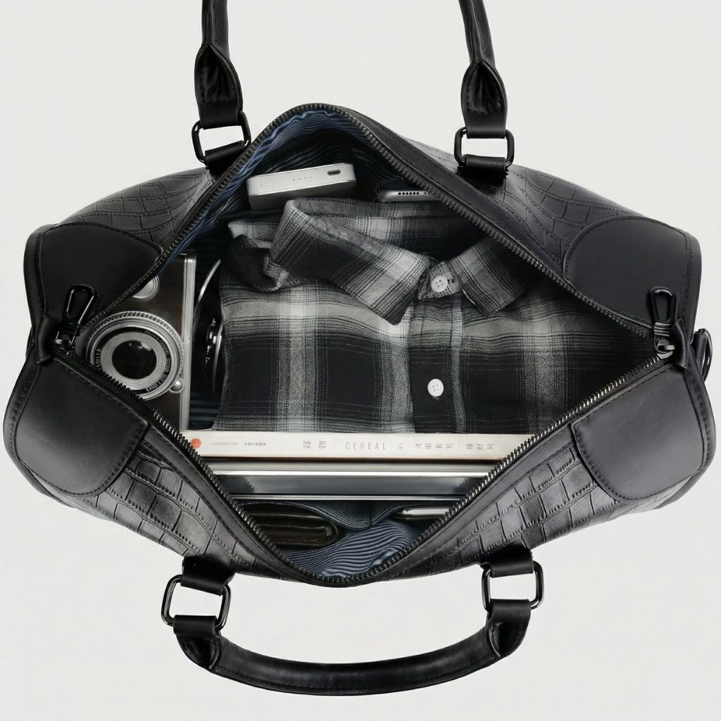 Vue de dessus du sac de voyage en cuir aspect croco noir ouvert, compartiment avec chemise, tablette et livres Image